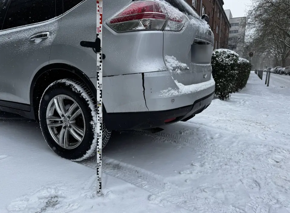 Riss im Heckstoßfänger eines Pkw, Schadenaufnahme mit Messlatte im Schnee